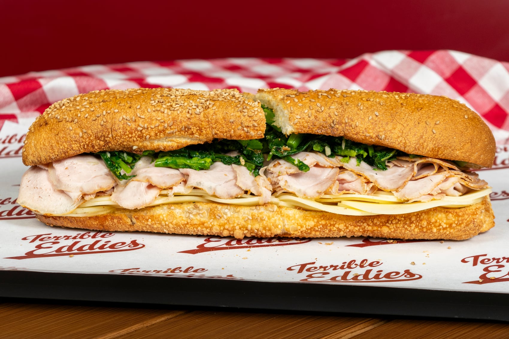 A loaded Terrible Eddie’s hero with sliced meat, greens, and cheese on a seeded roll